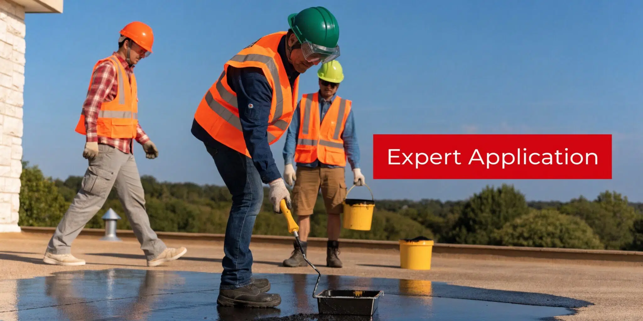 A team of construction workers in safety gear applying black waterproof coating to a flat rooftop.